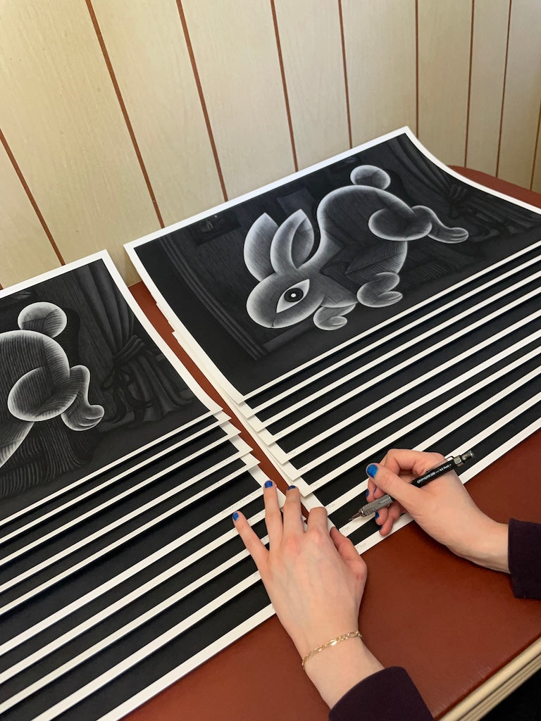 artist signing stacked black and white prints of a ghost rabbit floating in a living room