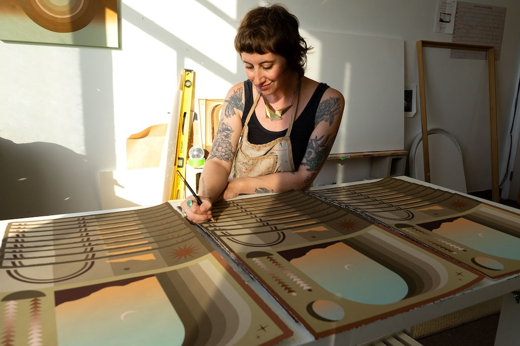 Woman with tattoos and apron signing fall equinox inspired prints in earthy brown tones