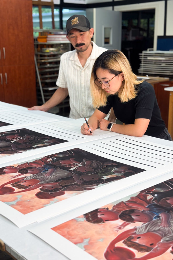 Two people signing prints of children  playing dodgeball at a table