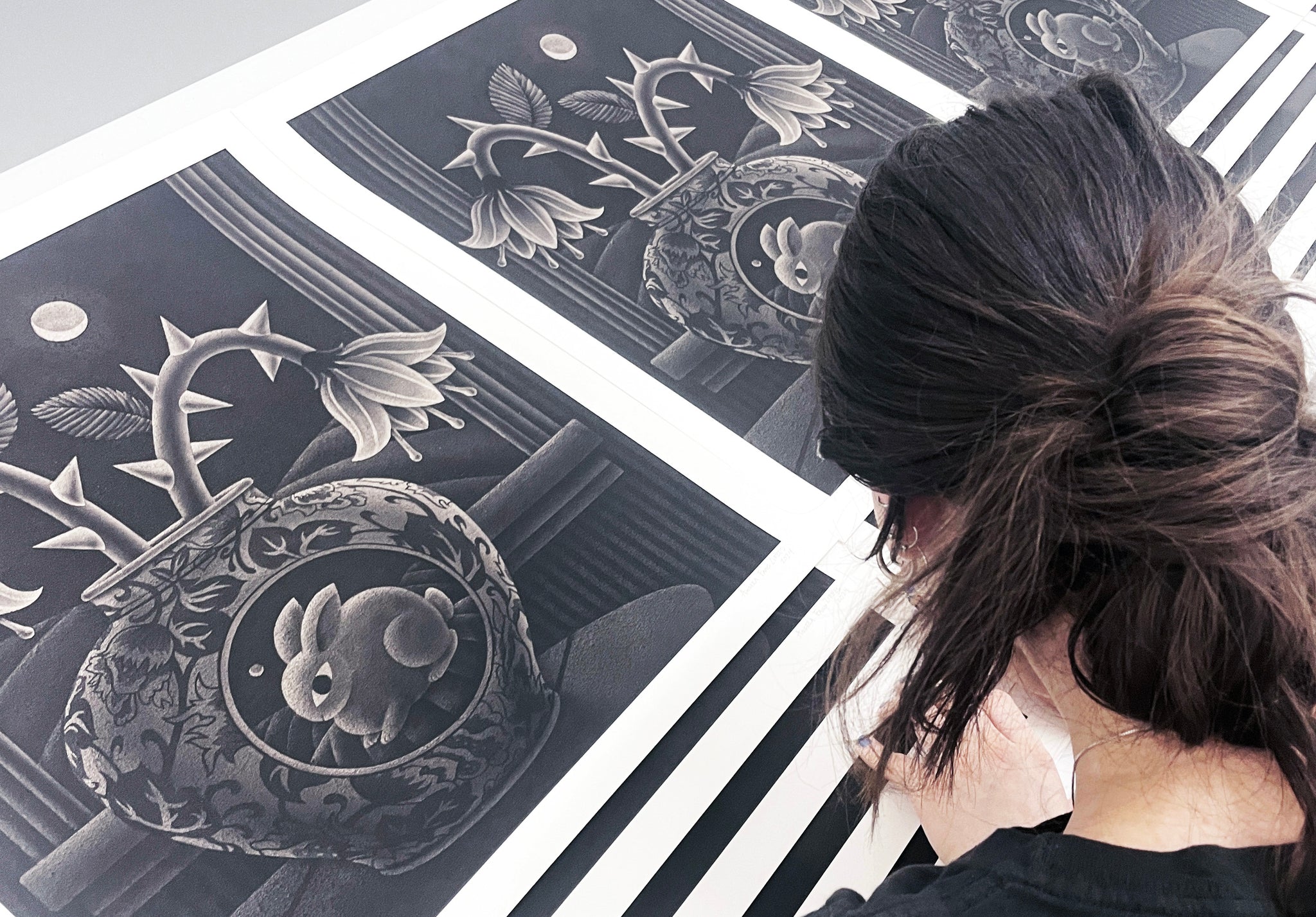 Angela Fang Zirbes signing prints - woman's head visible from behind bent over prints signing. Prints of rabbit on vase iwth moon in background