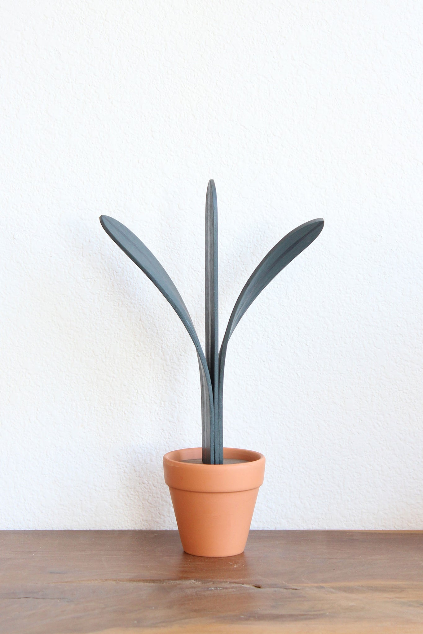 wooden sculpture of tall plant with three leafs in terracotta pot