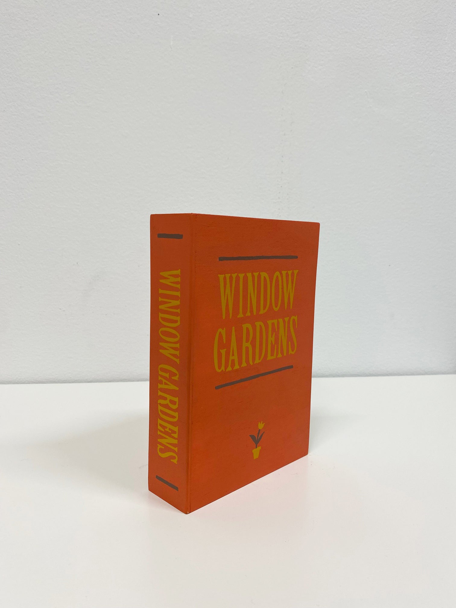 Wooden sculpture of a red book with the words Window Gardens on the front and on the spine of the book