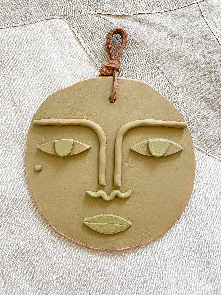 flat ceramic face with a cloth loop for hanging at the top