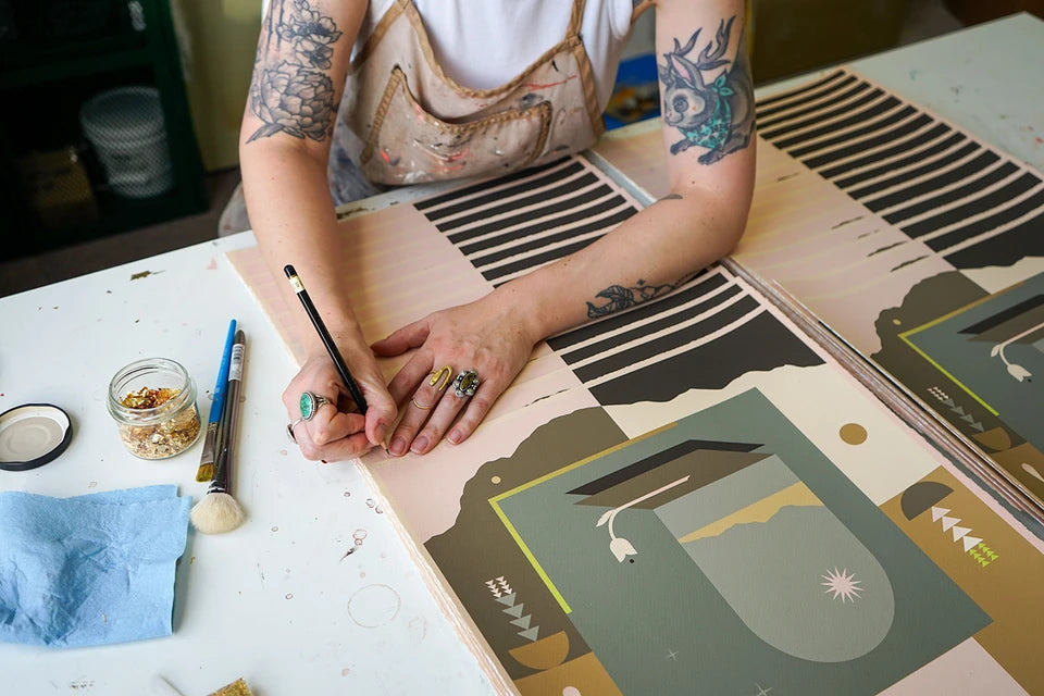 Woman with tattoos on arms and rings signing summer solstice inspired prints