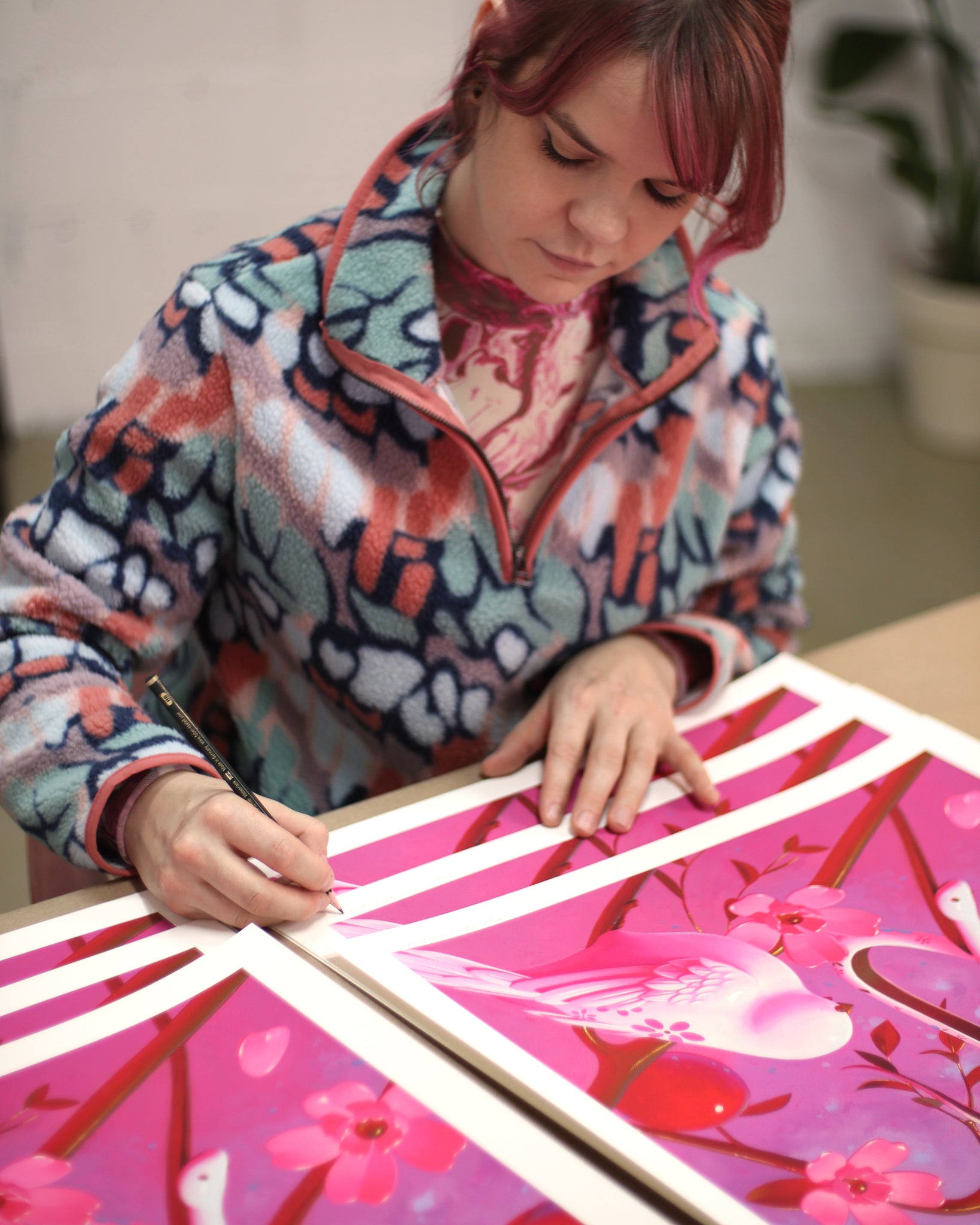 Megan Ellen MacDonald (woman with pink hair) signing prints of fruits on branches with porcelain birds and snake